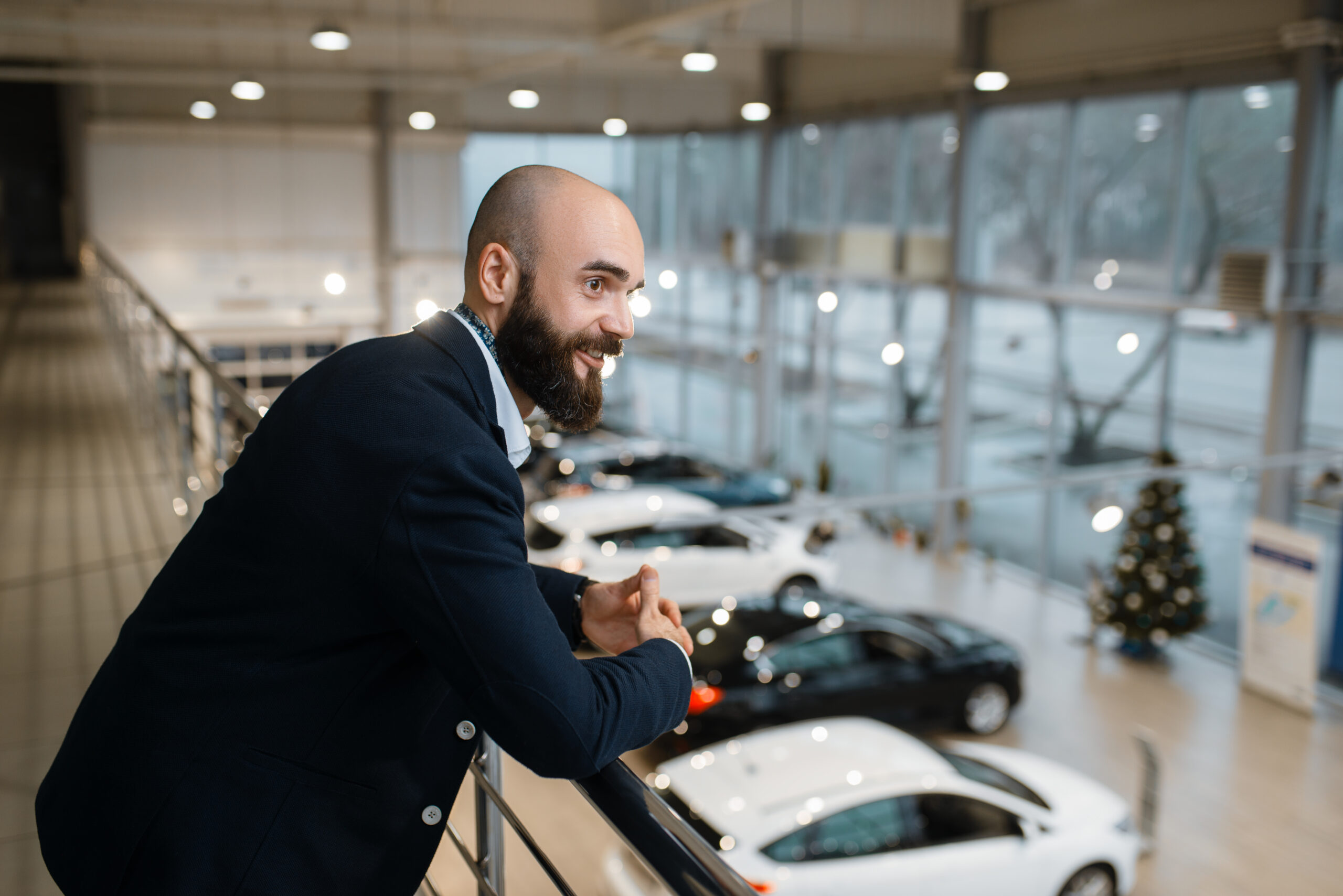 Happy businessman poses in car dealership. Customer in new vehicle showroom, male person buying automobile, auto dealer business